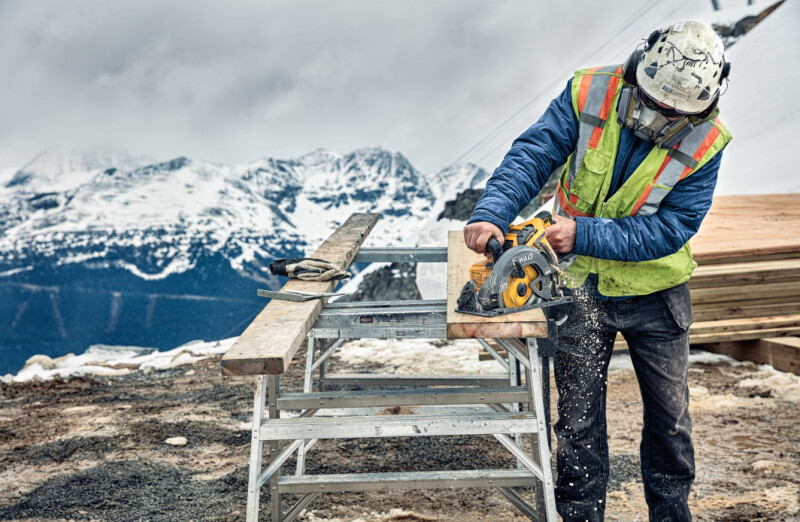 Close up of FLEXVOLT cordless worm drive style saw being used by person to cut wooden plank outdoors.