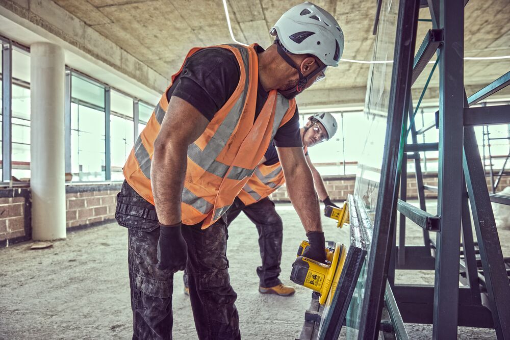 Two construction workers prepare to lift a large pane of glass using Grabo 18V XR Suction Lifters