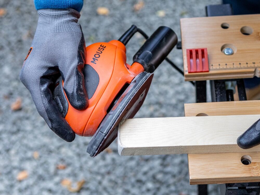 The edges of a wooden plank being rounded with the BLACK+DECKER 55W MOUSE Detail Sander.