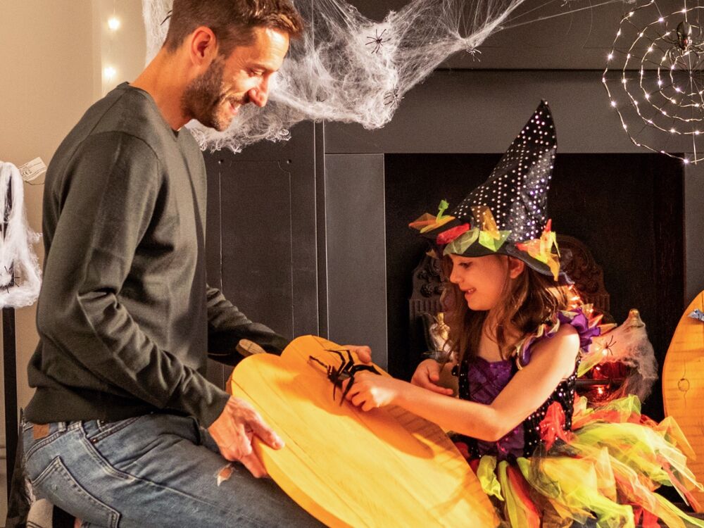 A father and young daughter decorate a wooden pumpkin.