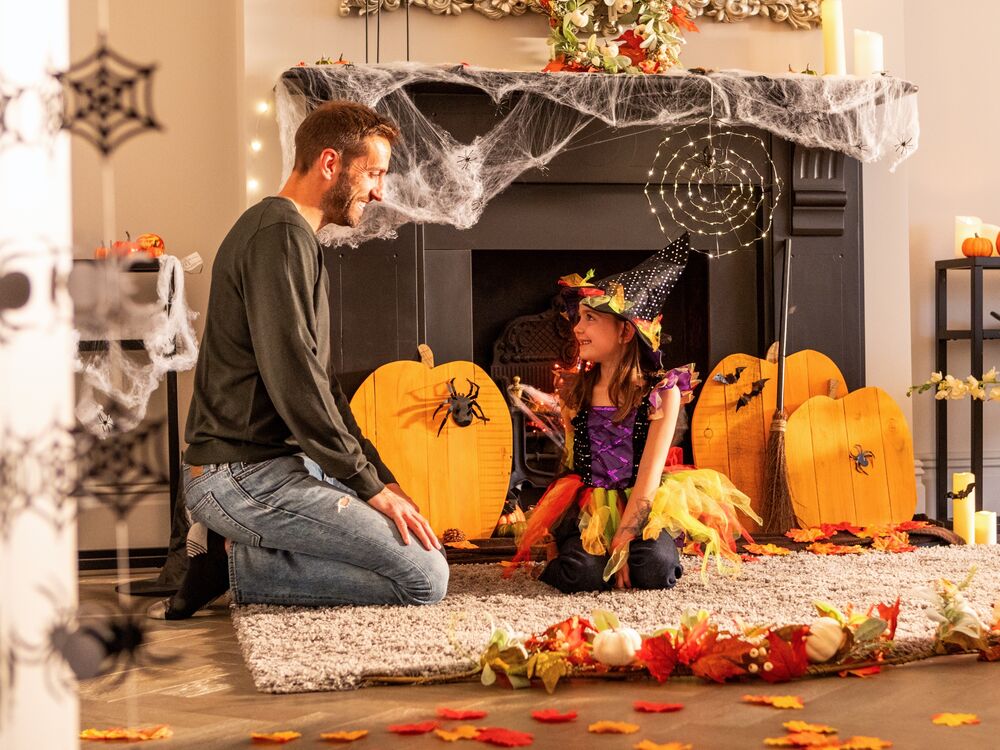 A father and young daughter celebrate halloween with wooden pumpkins.