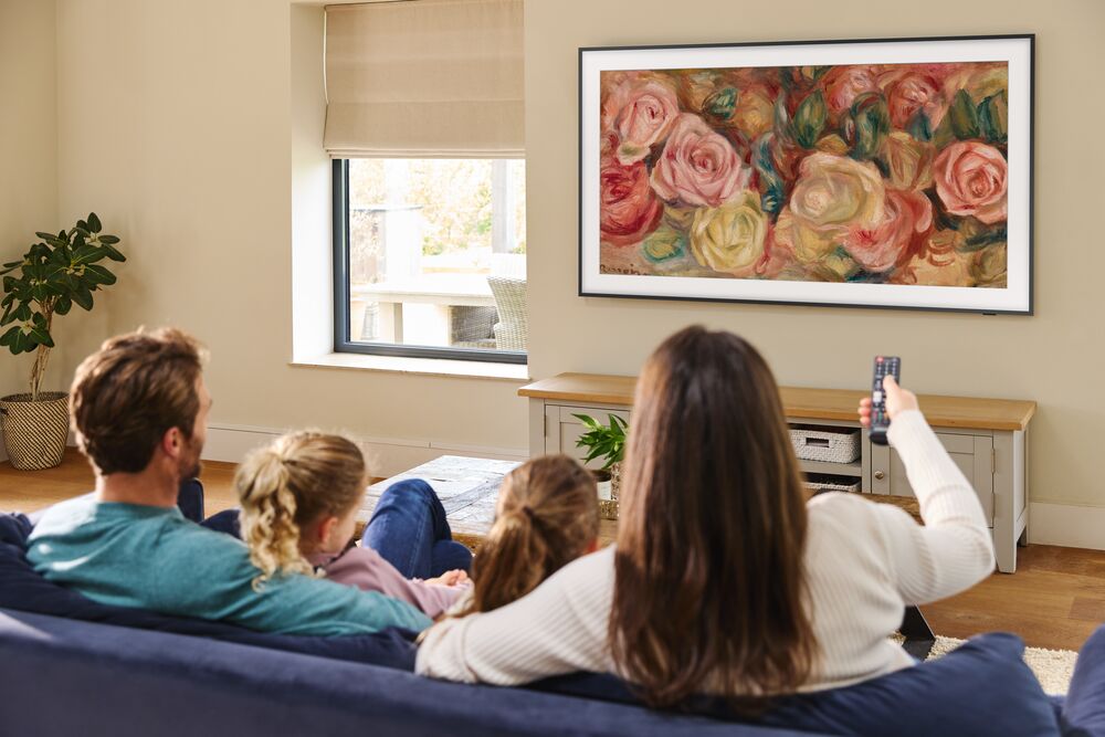 A family sit on a sofa to watch a Samsung 'The Frame' QLED Television.