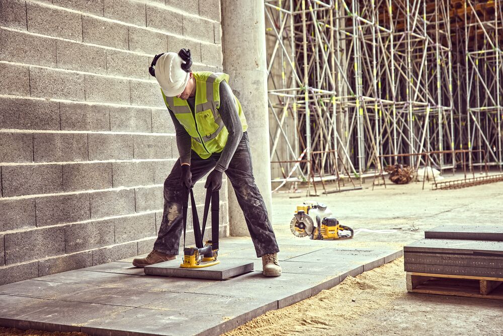 Construction worker uses the straps of a Grabo 18V XR Suction Lifter to lower a concrete block into position