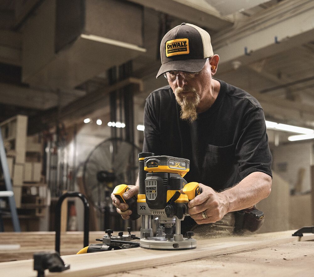 A tradesperson uses a DEWALT router on a piece of wood in a woodshop