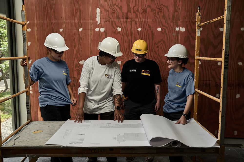 Four people in DEWALT gear discussing blueprints in an unfinished room