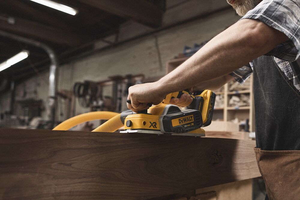 A tradesperson uses a DEWALT planer on a piece of wood