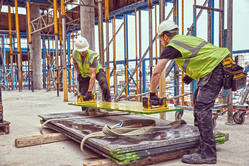 Two construction workers use Grabo 18V XR Suction Lifters to lift and lower a large plank of timber