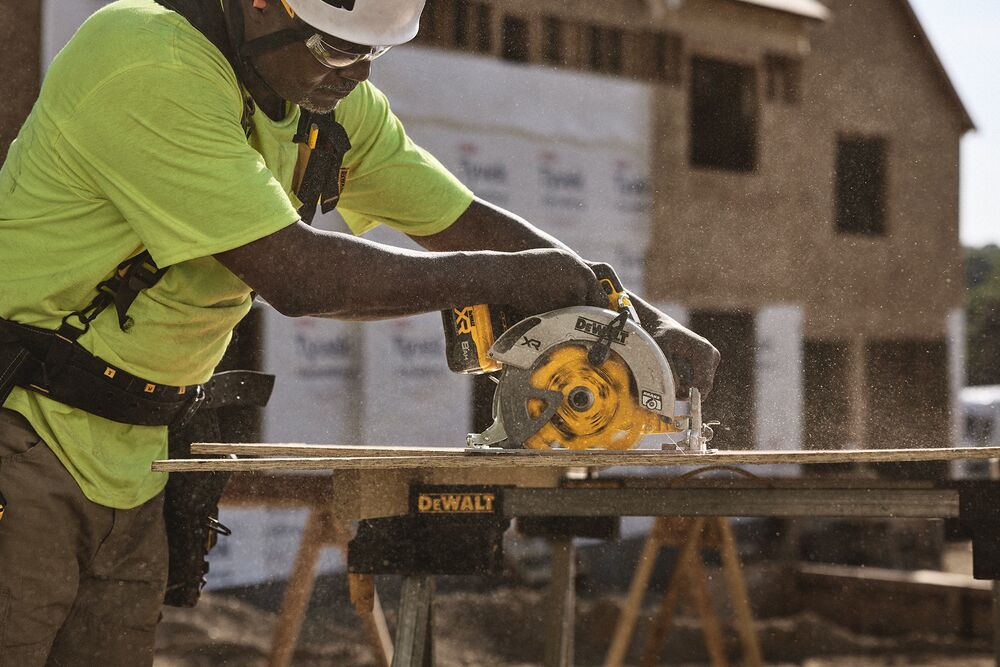 A tradesperson uses a DEWALT circular saw to cut a sheet of wood