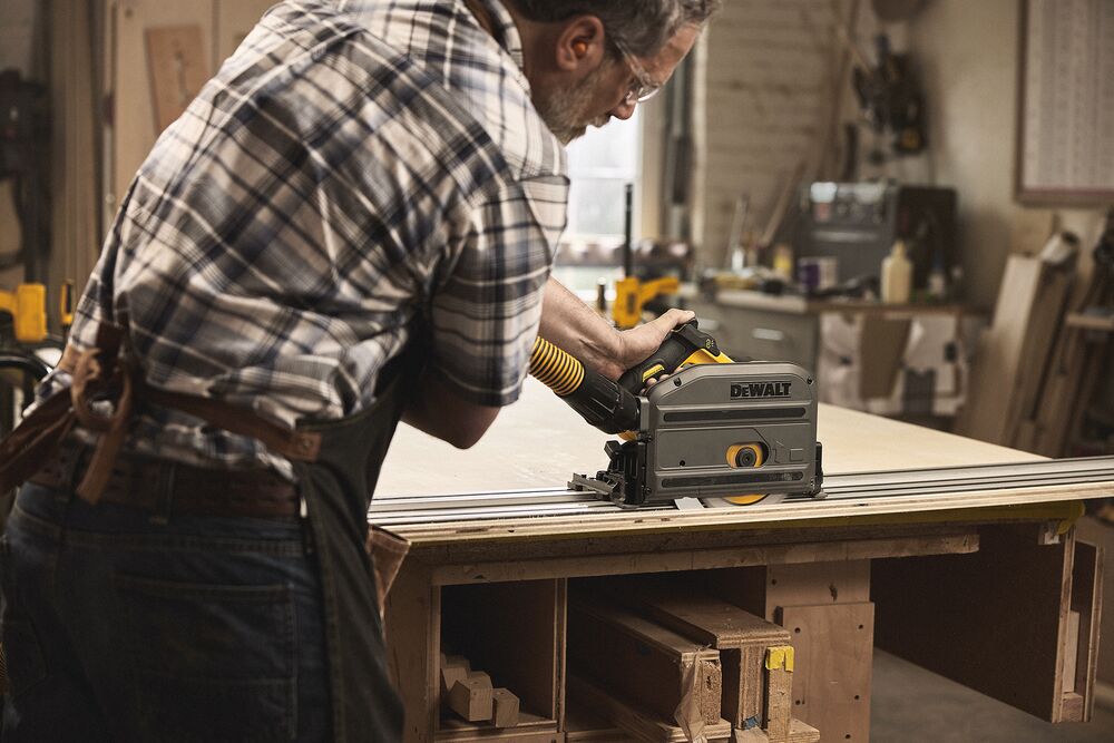 A tradesperson uses a DEWALT circular saw with a hose to cut a sheet of wood