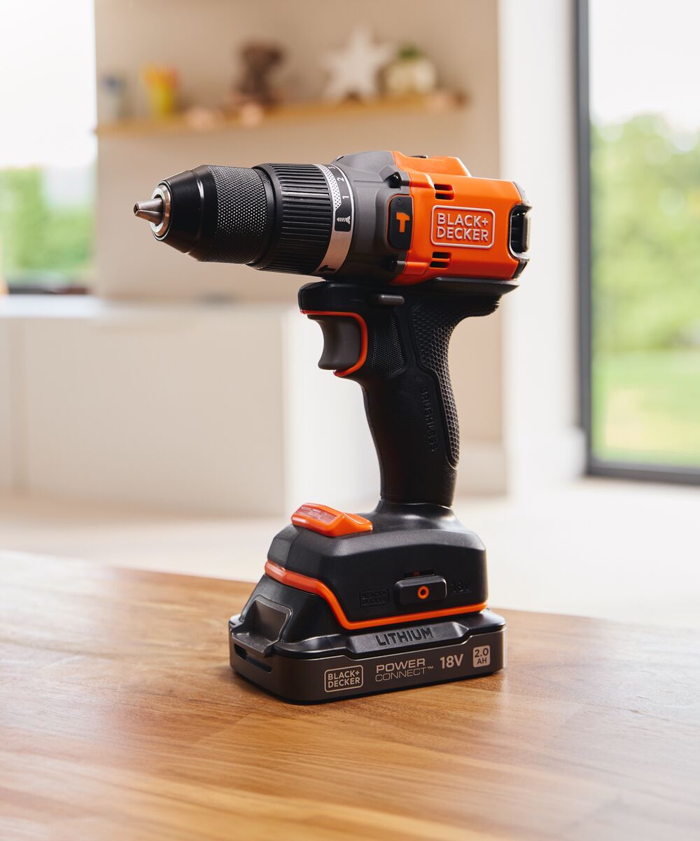 The BLACK+DECKER® 18V POWERCONNECT™ Brushless Hammer Drill standing on a living room table.