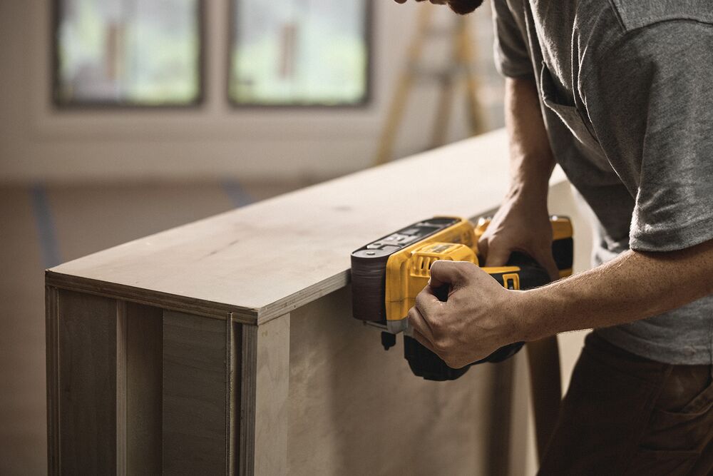 A tradesperson uses a DEWALT belt sander to finish a cabinet