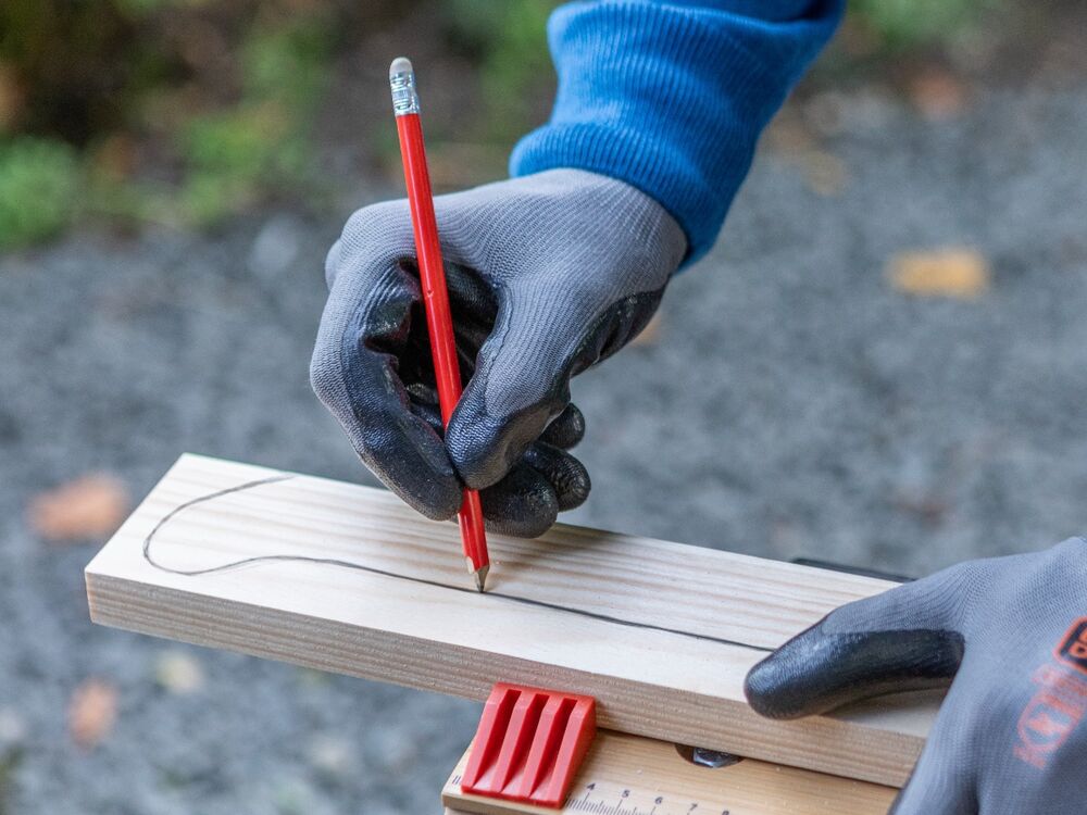 An outline of a sleigh blade being drawn on a wooden plank.