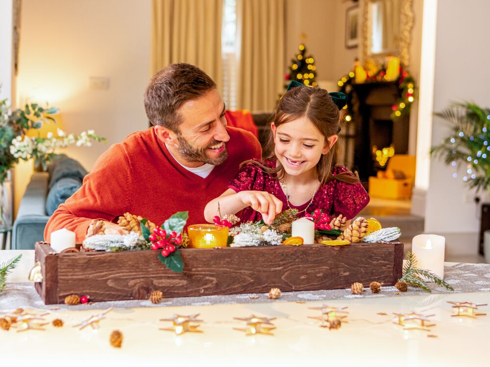 A father and young daughter decorate a festive wooden candle holder.