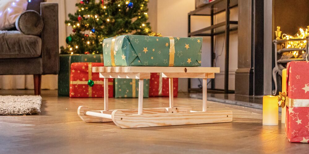 A wooden mini sleigh surrounded by Christmas presents in a living room.