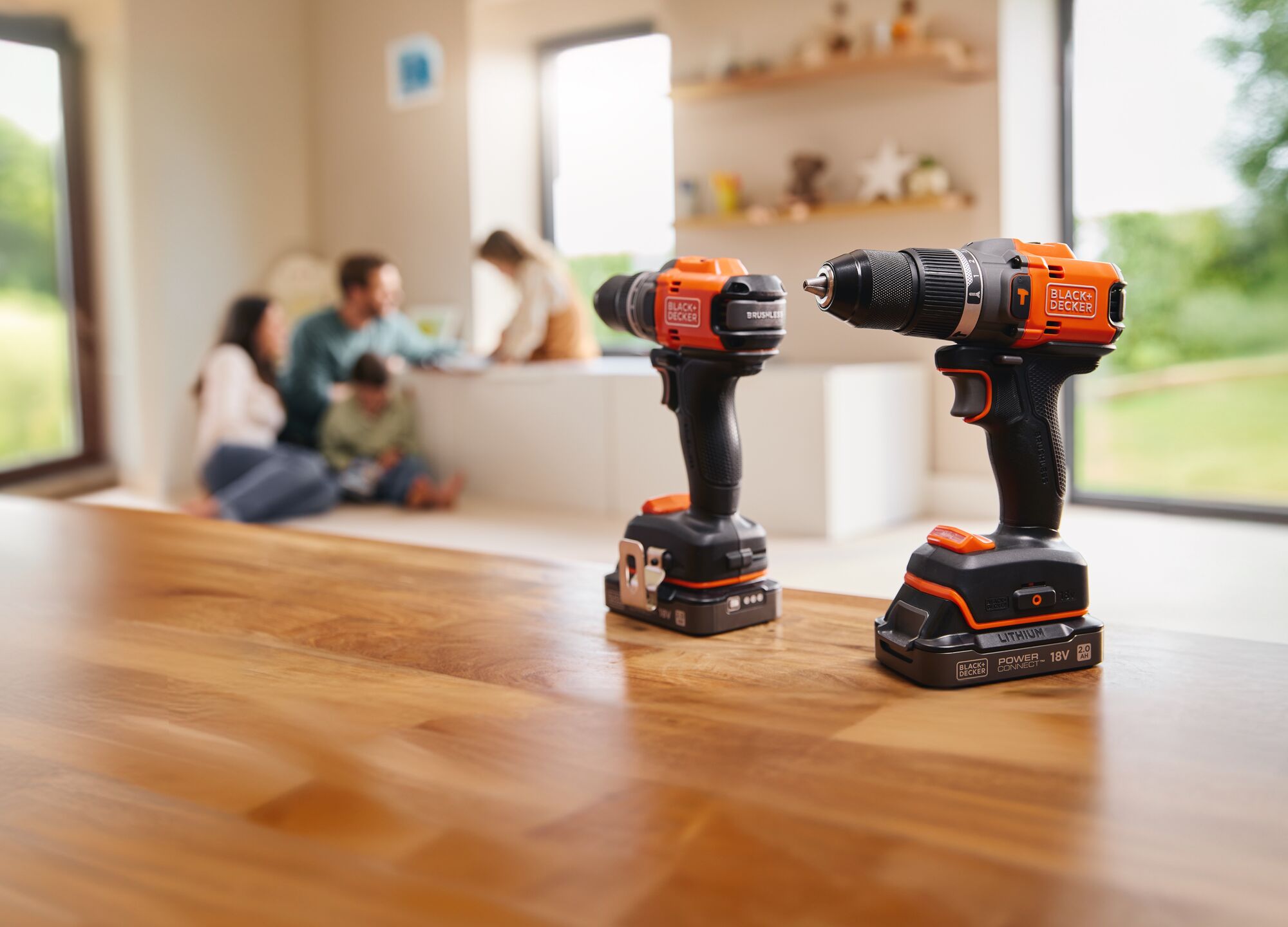 The BLACK+DECKER® 18V POWERCONNECT™ Brushless Hammer Drill and Drill Driver standing on a living room table with a family in the background.