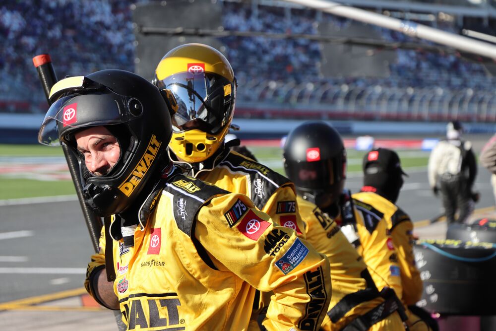 Four people in DEWALT racing suits stand at the ready during a race