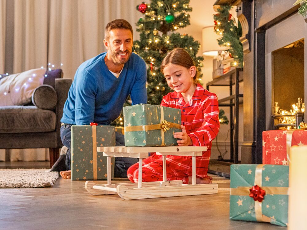 A father and young daughter with a wooden mini sleigh and Christmas presents.