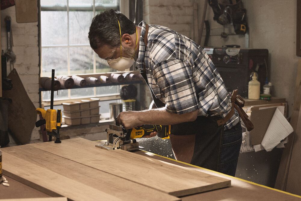 A tradesperson uses a DEWALT circular saw with a hose to cut a sheet of wood