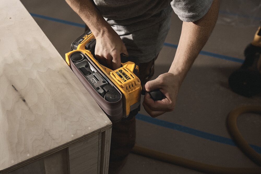 A tradesperson uses a DEWALT belt sander to finish a cabinet