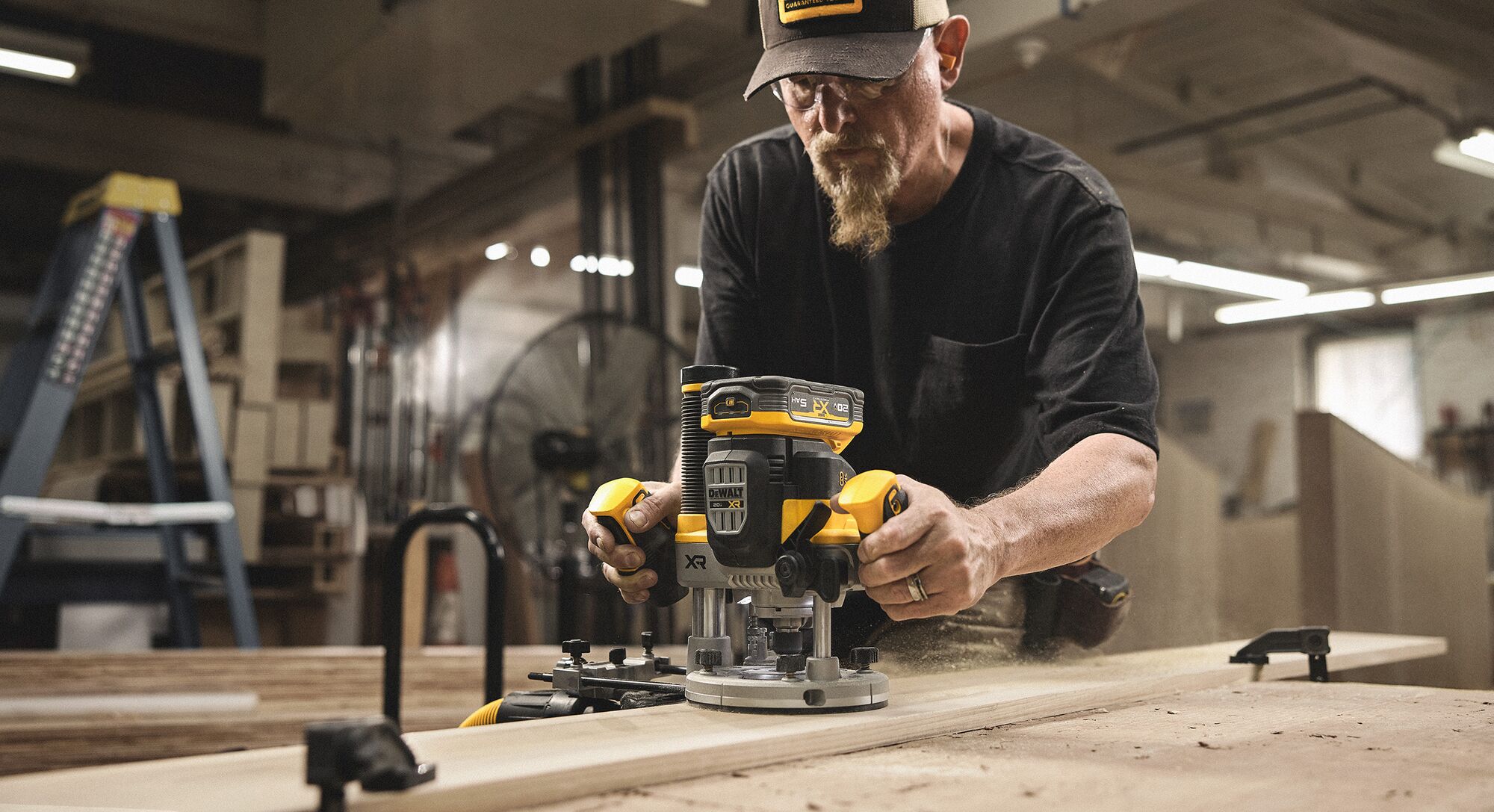 A tradesperson uses a DEWALT router on a piece of wood in a woodshop