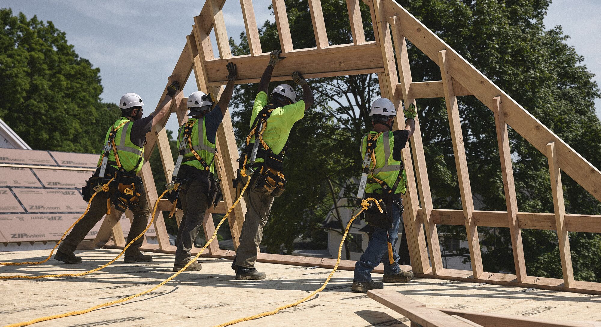 Four tradespeople hoist a sloped frame upwards