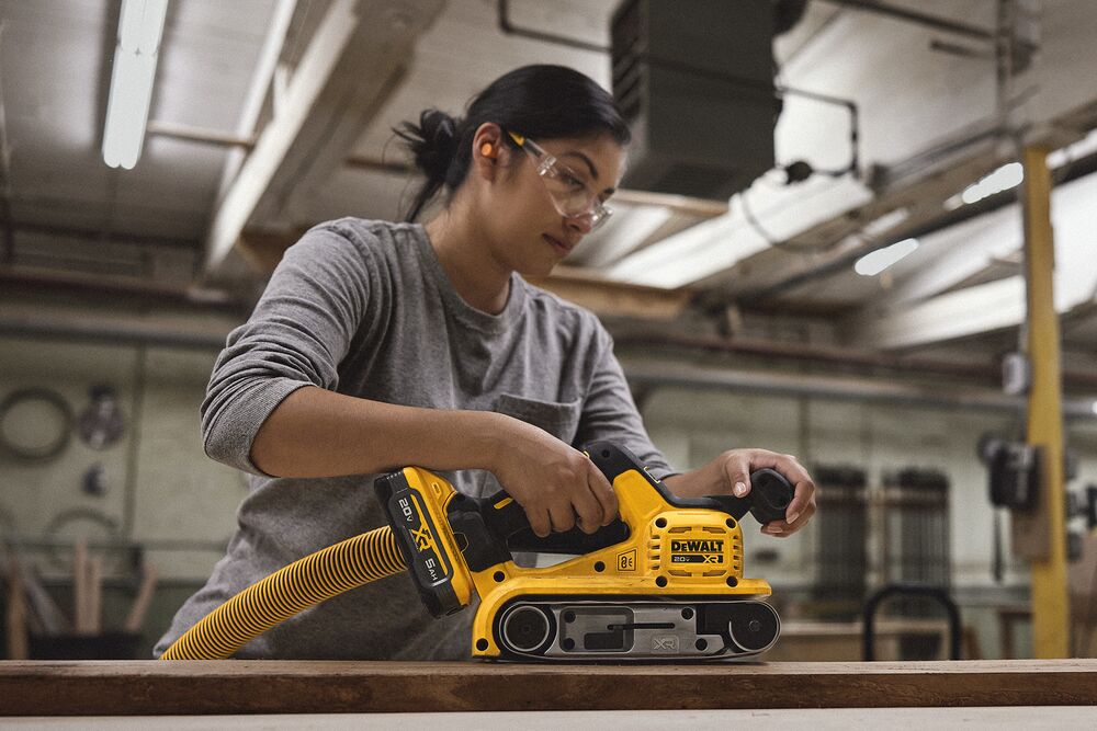 A tradesperson uses a DEWALT belt sander with a hose to finish a piece of wood