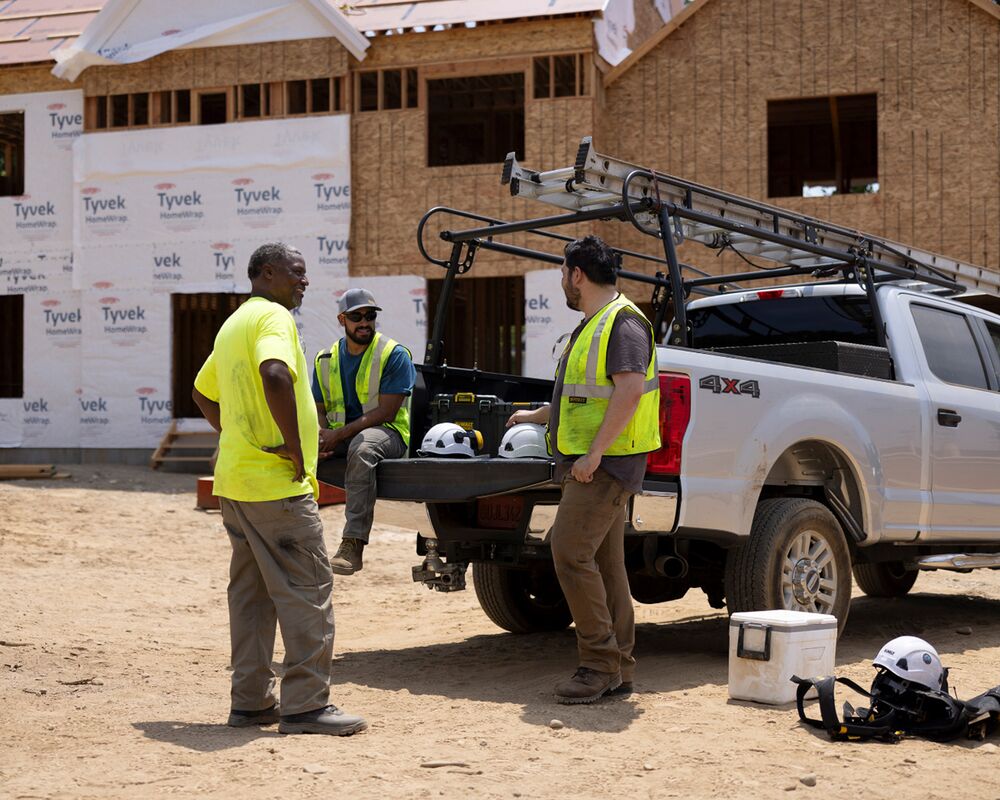 A group of tradespeople gather around the bed of a pick-up truck